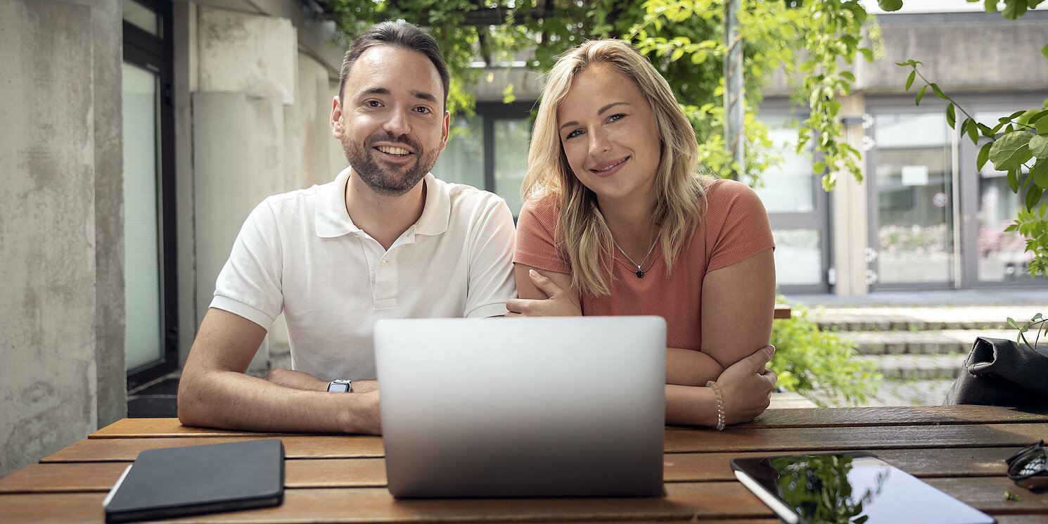 Ein Mann und eine Frau sitzen in einem Innenhof vor einem Laptop