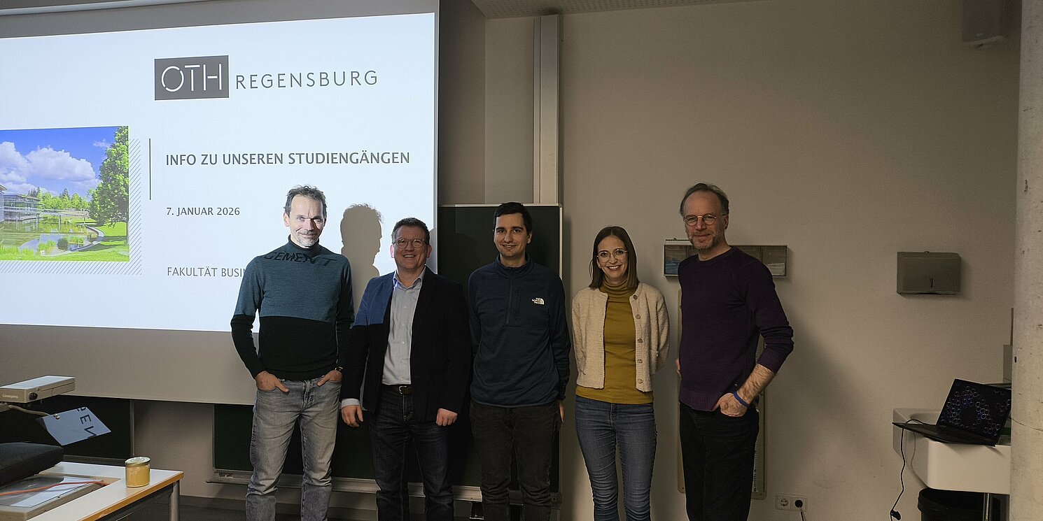 4 Personen stehen im Raum, in Hintergrund eine Prsäsentation