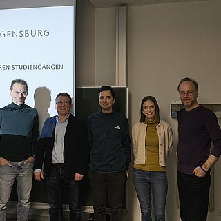 4 Personen stehen im Raum, in Hintergrund eine Prsäsentation