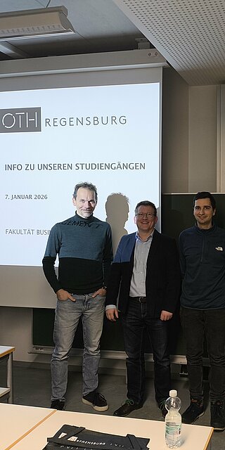 4 Personen stehen im Raum, in Hintergrund eine Prsäsentation